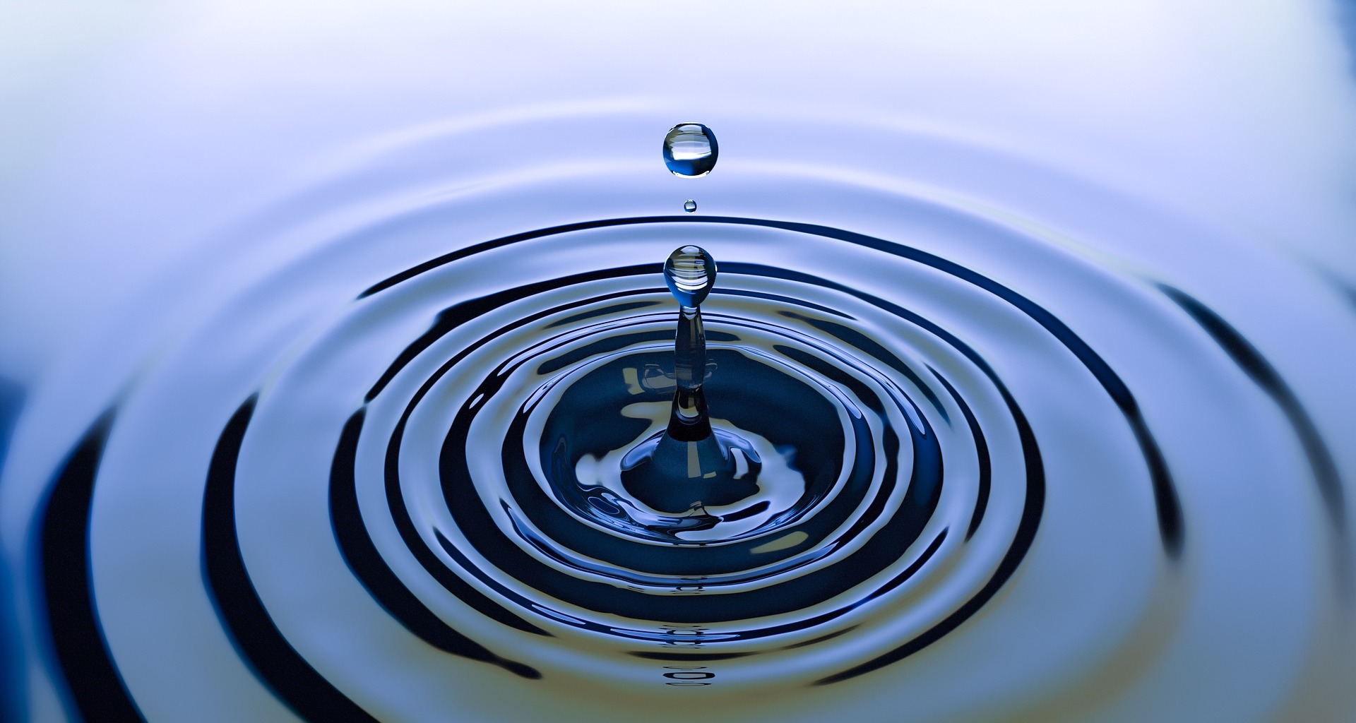 A water drop falls in a body of water, leaving a ripple effect.